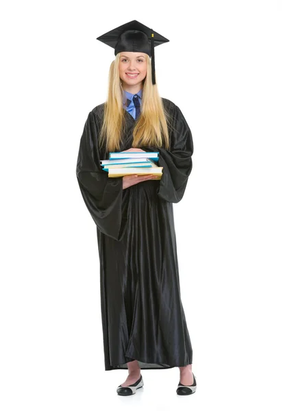 Full length portrait of young woman in graduation gown with stac — Stock Photo, Image