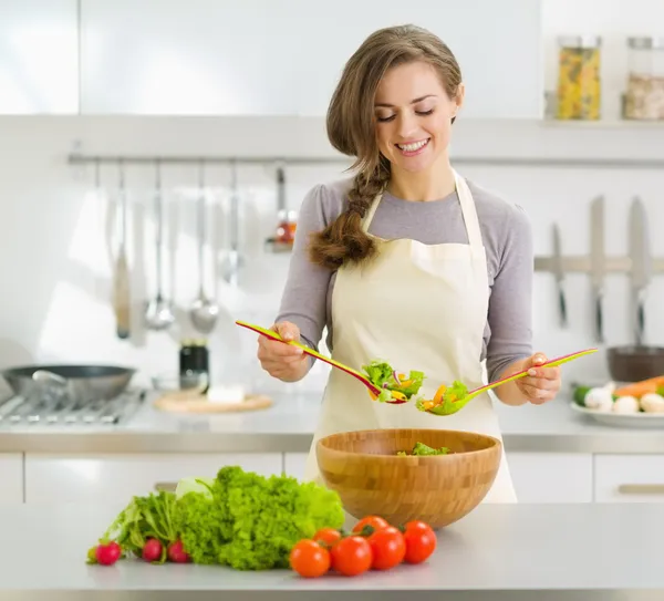 Lachende jonge huisvrouw mengen van verse salade — Stockfoto