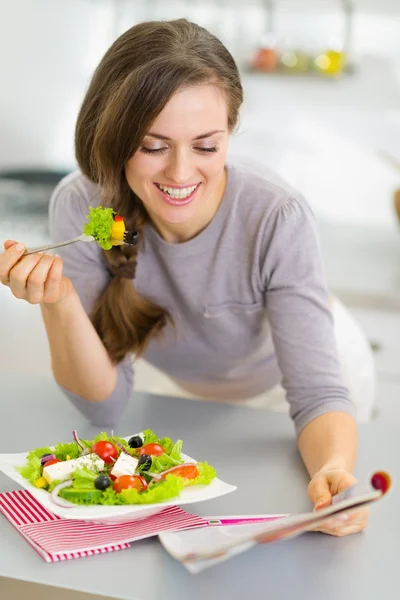 Glad ung hemmafru äta färsk sallad och läsa tidningen i — Stockfoto