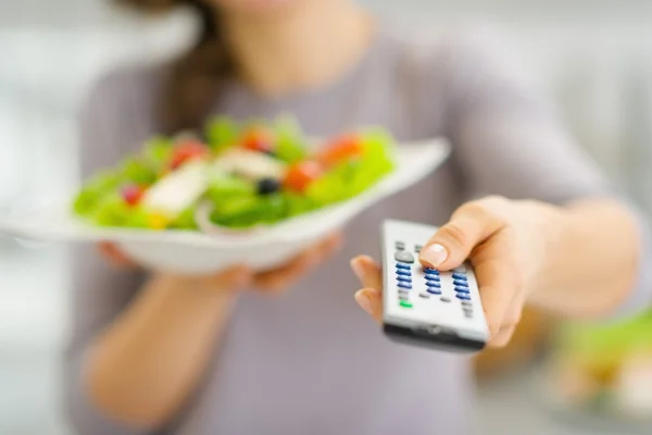 Closeup on tv remote control and fresh salad in hand of young wo — Stock Photo, Image