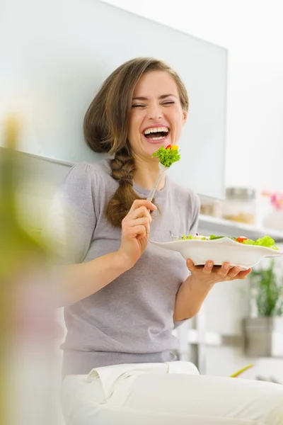 Sorridente giovane donna mangiare insalata fresca in cucina moderna — Foto Stock