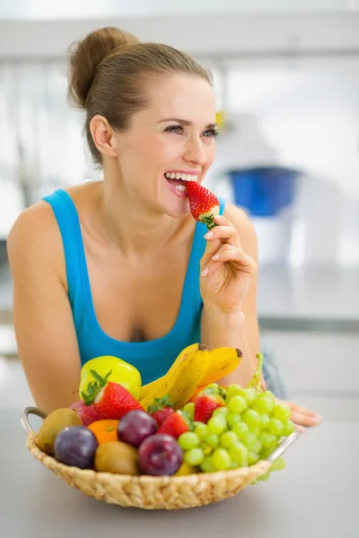 Feliz joven mujer comiendo fresa en la cocina moderna — Foto de Stock