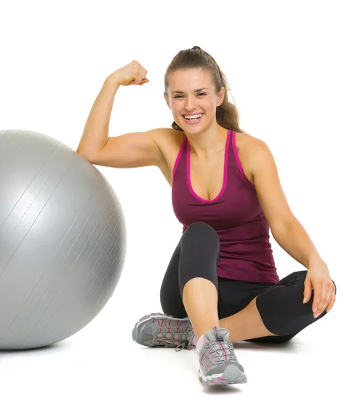 Feliz fitness joven sentada cerca de la pelota de fitness y mostrando —  Fotos de Stock