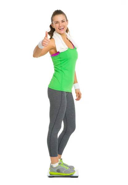 Smiling fitness young woman standing on scales and showing thumb — Stock Photo, Image