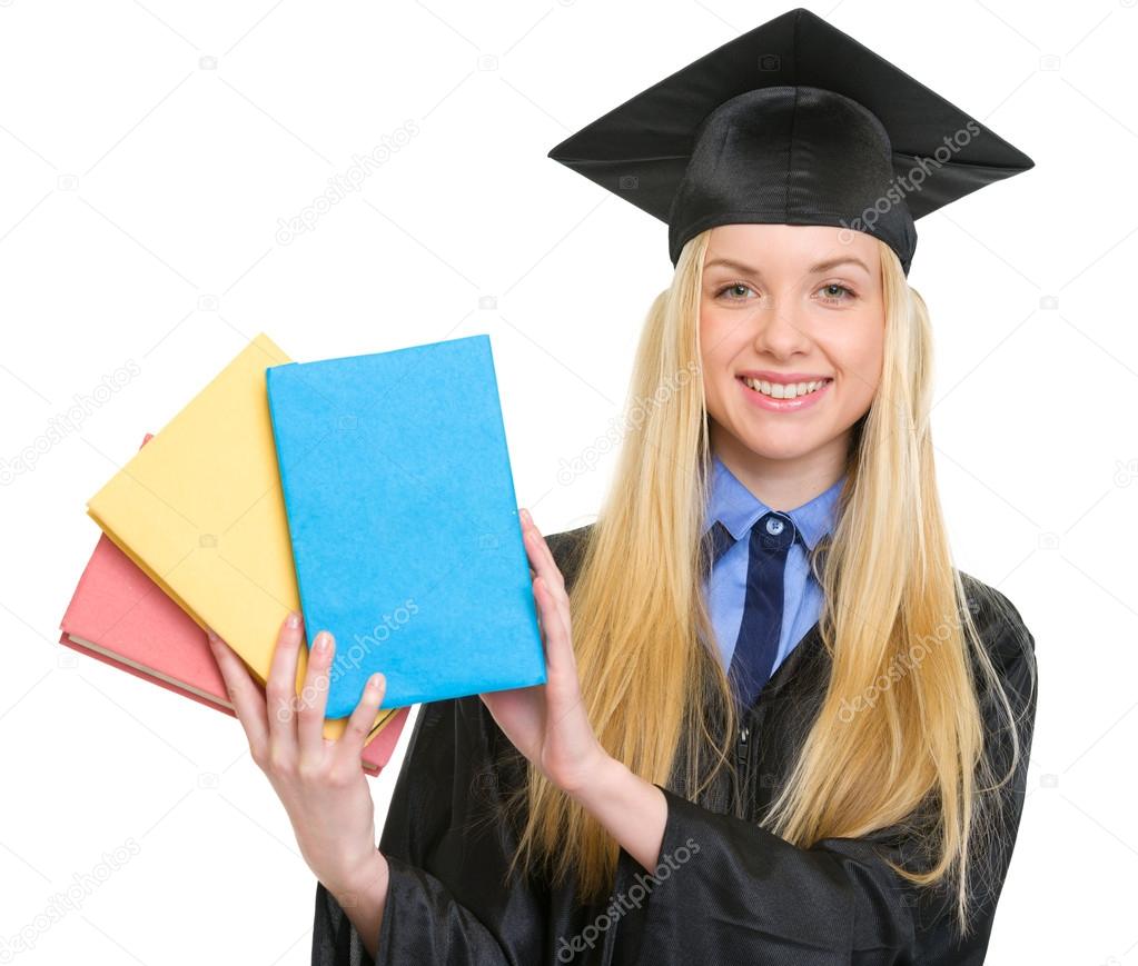Smiling young woman in graduation gown showing books