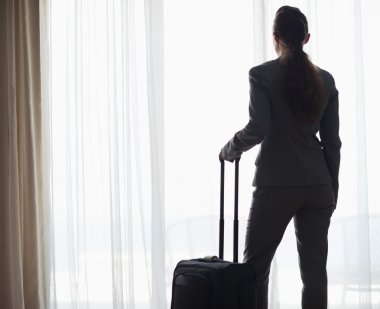 hotel penceresine bakarak tekerlekli çanta ile iş kadın silüeti