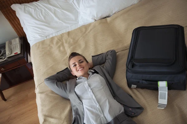 Smiling business woman laying on bed in hotel room — Stock Photo, Image