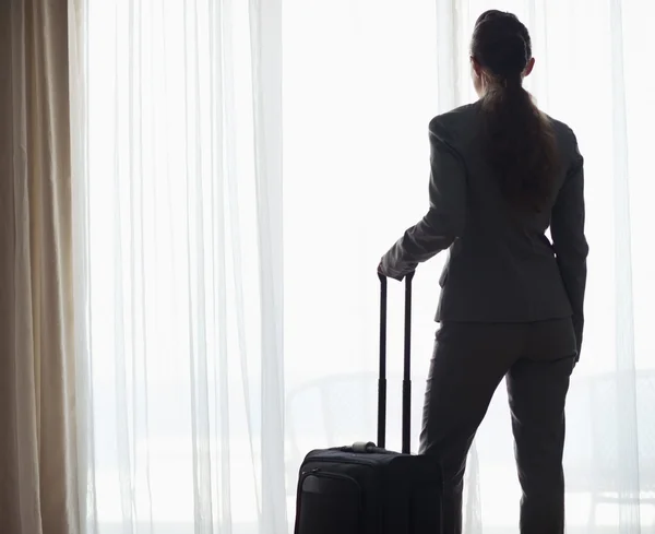 Silhouette of business woman with wheel bag looking into hotel window — Stock Photo, Image