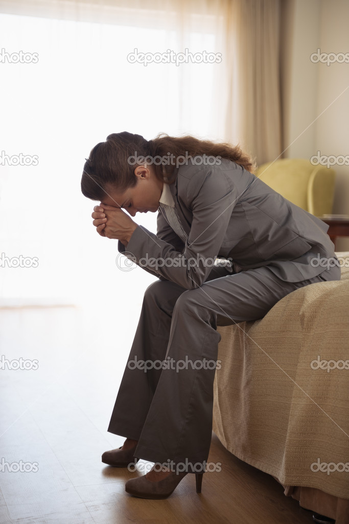 Concerned business woman sitting on bed in hotel room