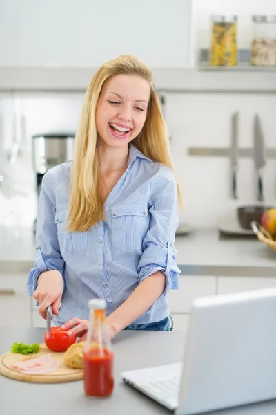 Tiener meisje maken sandwich in keuken en op zoek in laptop — Stockfoto