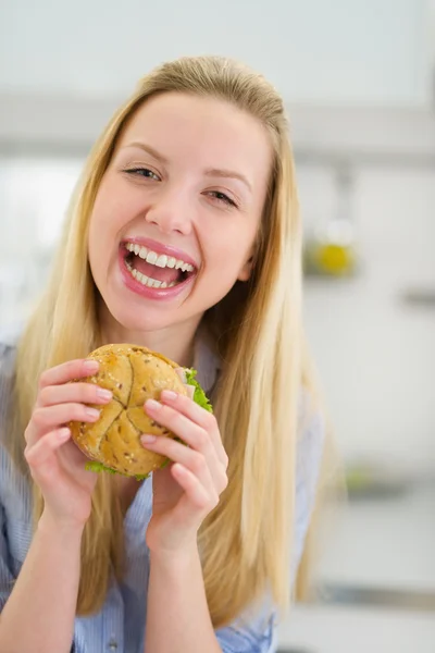 Sorrindo adolescente menina comendo sanduíche na cozinha — Fotografia de Stock