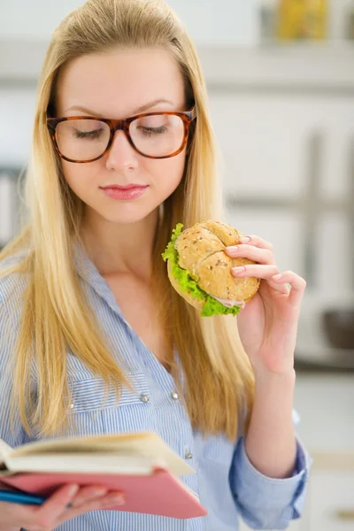 Jonge vrouw eten sandwich en leesboek — Stockfoto