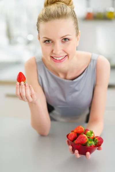 Heureuse jeune femme au foyer mangeant des fraises dans la cuisine — Photo