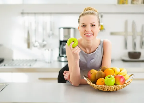 Jovem dona de casa feliz com maçã na cozinha moderna — Fotografia de Stock