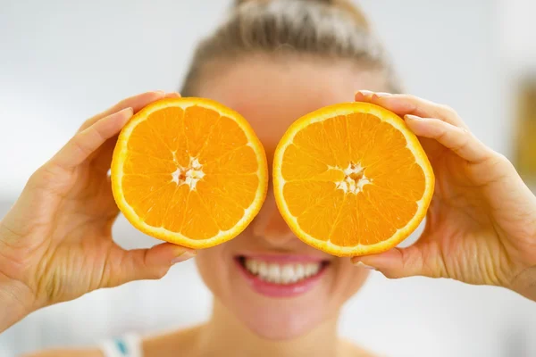 Jovencita feliz sosteniendo dos rebanadas de naranja delante de los ojos —  Fotos de Stock