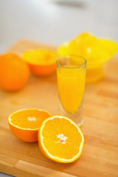 Gros plan sur verre de jus d'orange et d'oranges sur planche à découper — Photo