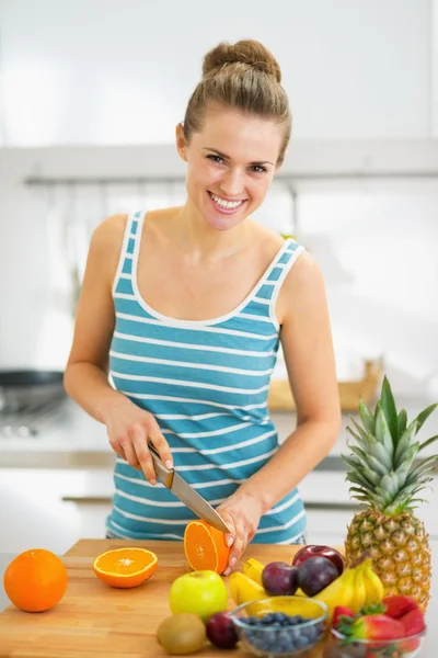 Šťastná mladá žena řezací oranžová v moderní kuchyni — Stock fotografie