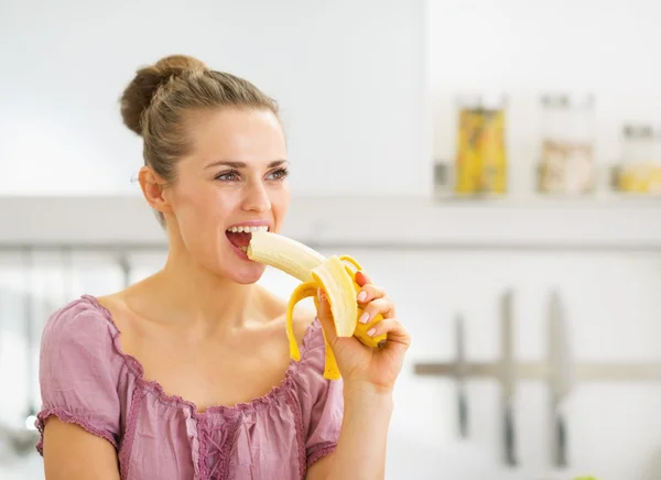 Mladá žena jíst banán v kuchyni — Stock fotografie