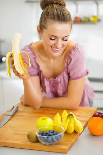 Glücklich junge Hausfrau essen Banane in der Küche — Stockfoto