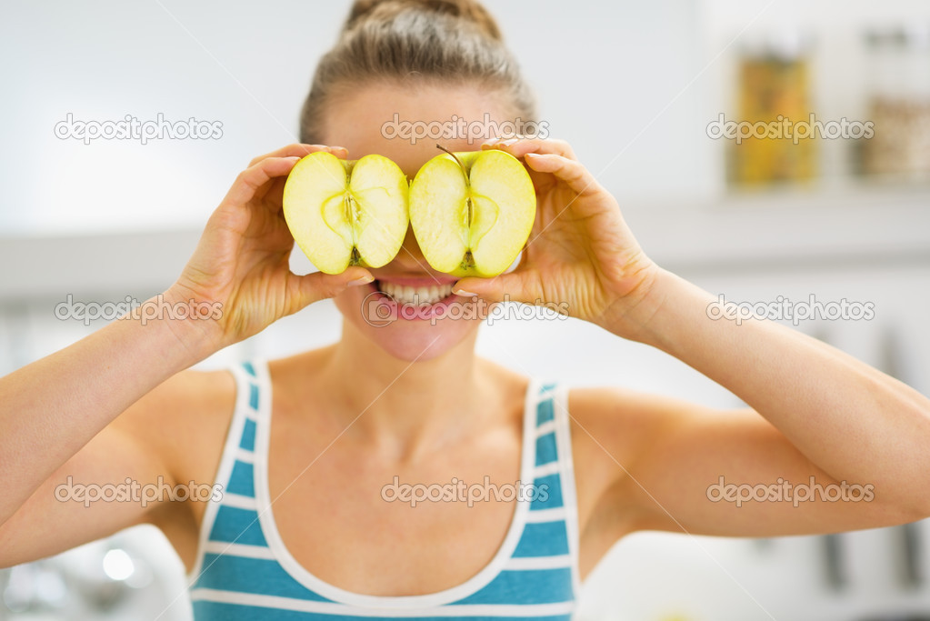 Happy young woman holding two slices of apple in front of eyes