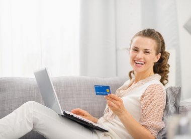 mutlu genç ev hanımı laptop ve kredi kartı ile koltuk döşeme