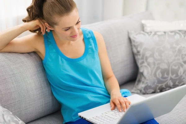 Doordachte jonge vrouw zittend op de Bank en met behulp van laptop — Stockfoto