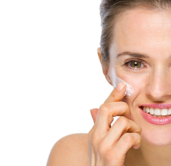 Closeup on happy young woman applying creme on cheek