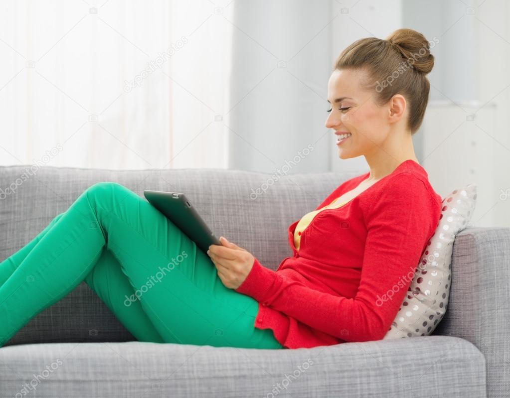 Smiling young woman sitting on divan and using tablet pc