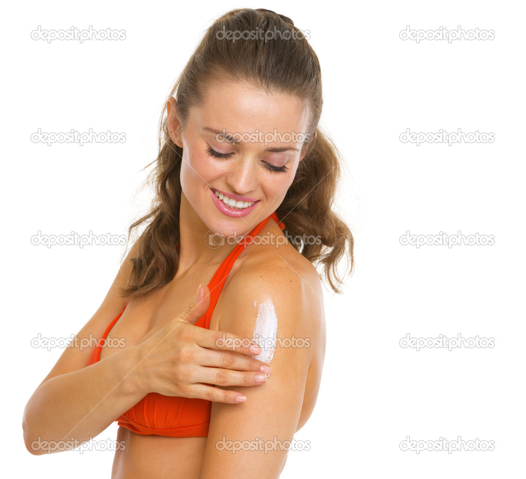 Happy young woman in swimsuit applying sun block creme