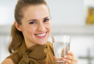 Portrait of happy young woman drinking water in kitchen clipart