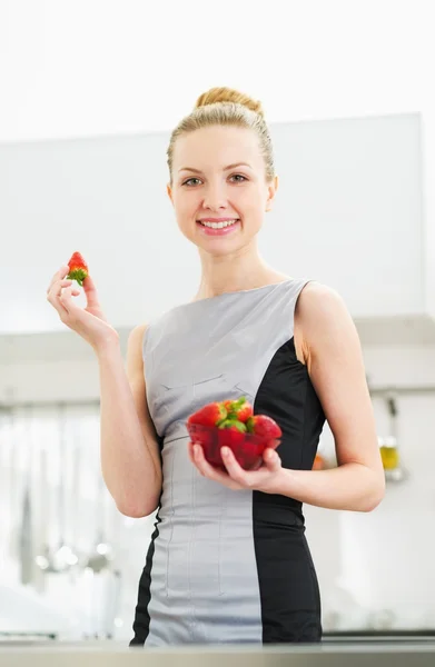 Jonge huisvrouw eten aardbei in moderne keuken — Stockfoto