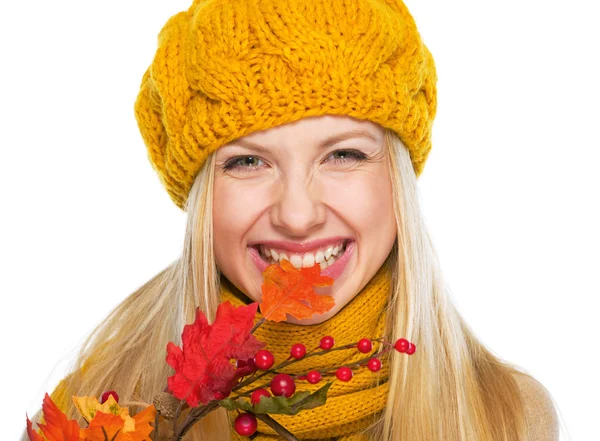 Smiling girl in hat and scarf biting autumn leaf — Stock Photo, Image