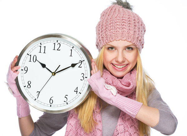 Happy teenager girl in winter hat and scarf showing clock