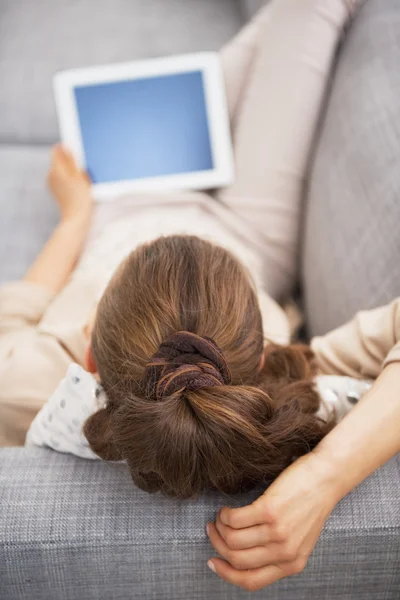 Young woman laying on sofa with tablet pc . rear view — Stock Photo, Image