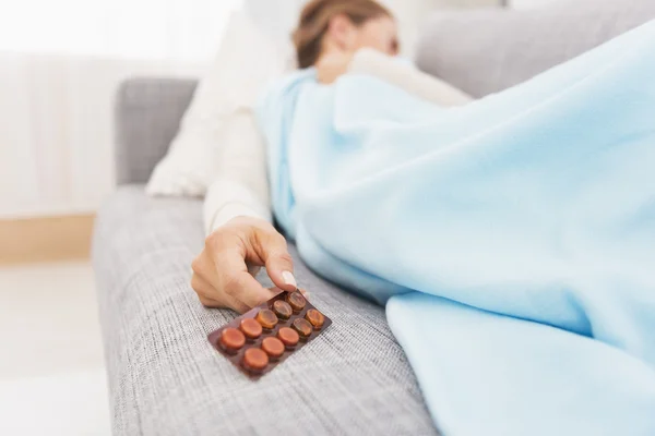 Zbliżenie na opakowanie tabletek w ręku źle młoda kobieta na kanapie — Zdjęcie stockowe