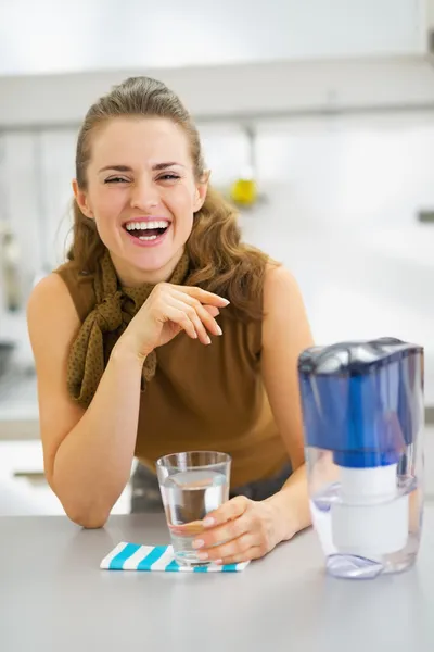 Счастливая молодая домохозяйка пьет воду из кувшина с фильтром — стоковое фото