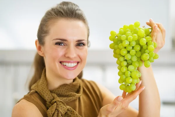 Retrato de jovem dona de casa sorrindo mostrando ramo de uvas — Fotografia de Stock