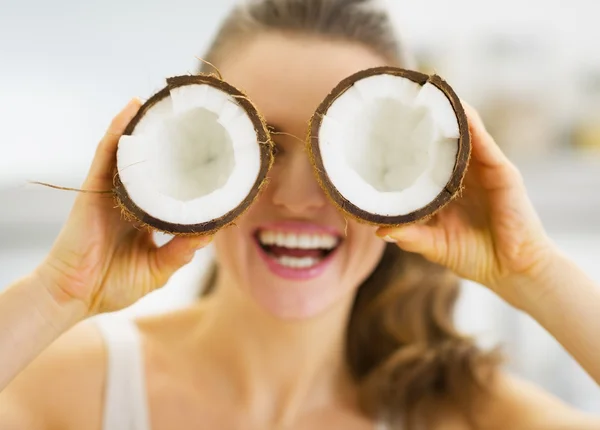 Smiling young woman holding two pieces of coconut in front of ey — Stock Photo, Image