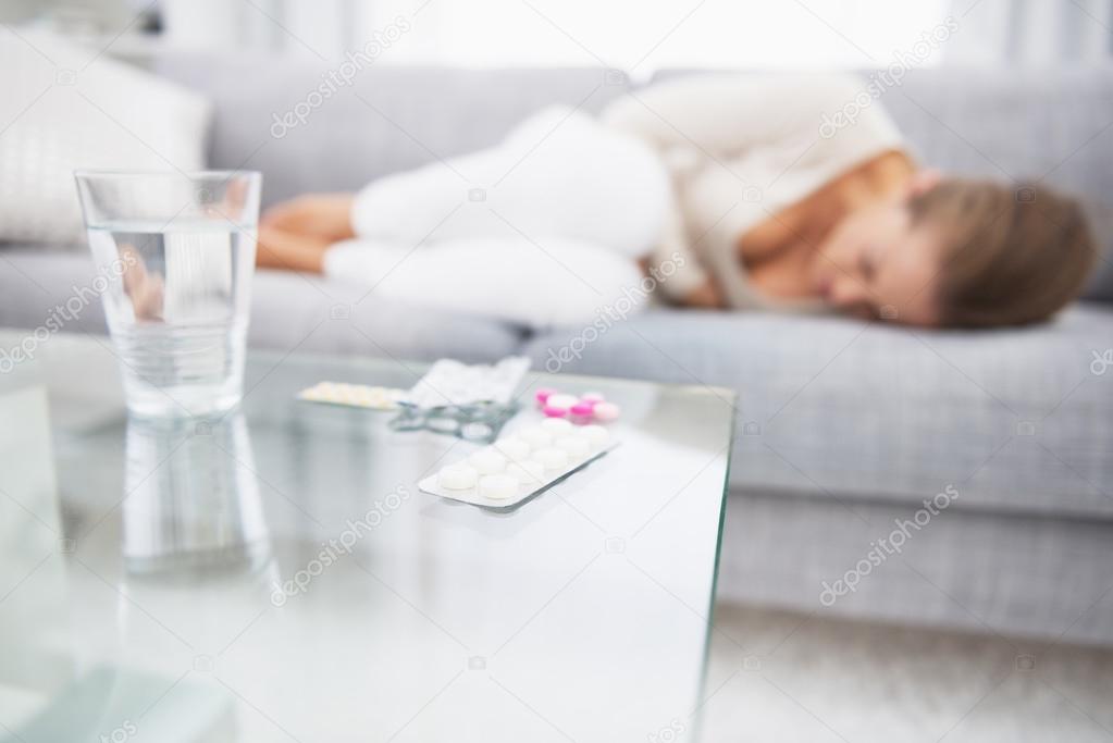 Closeup on medicine on table and feeling bad young woman in back