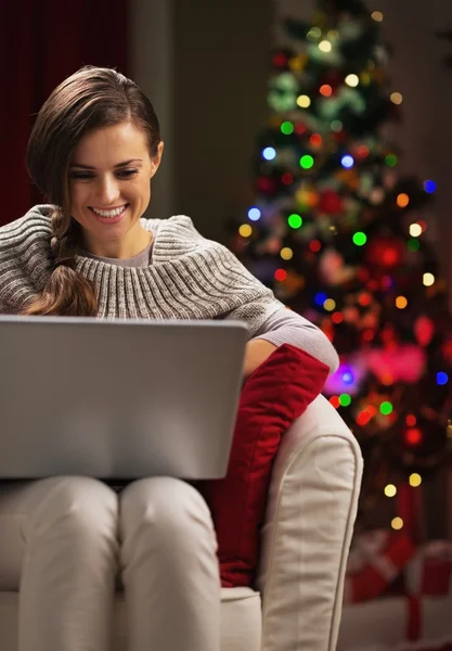 微笑的年轻女士使用的便携式计算机的圣诞节树附近 — 图库照片