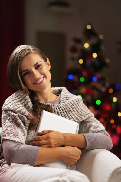 快乐的年轻女人拥抱 tablet pc 的圣诞节树附近 — 图库照片