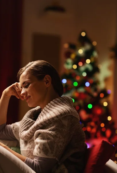 Drömmer unga kvinna som sitter i fåtölj framför jul t — Stockfoto
