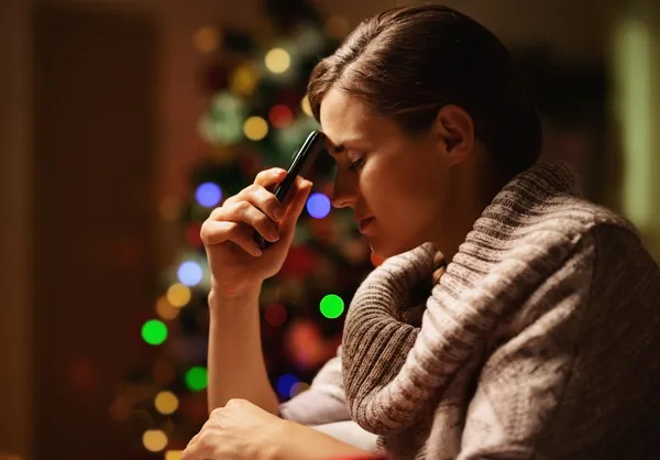 Mujer joven preocupada con teléfono móvil delante de la Navidad tr — Foto de Stock