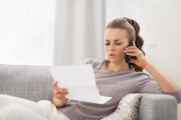 Concerned young woman with letter and talking cell phone — Stock Photo, Image