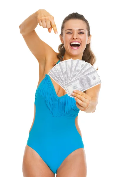 Smiling young woman in swimsuit pointing on fan of dollars — Stock Photo, Image