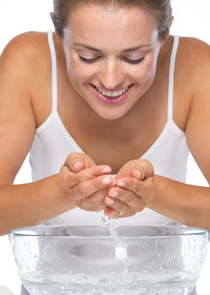 Glad ung kvinna tvättar ansiktet i skål med vatten — Stockfoto