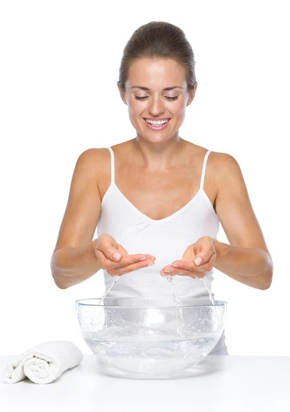 Улыбающаяся молодая женщина моет руки в стеклянной чаше с водой — стоковое фото