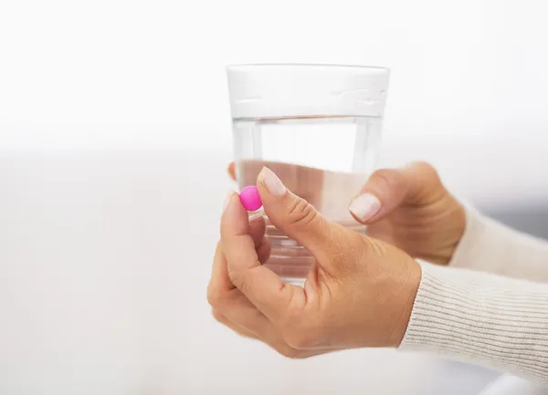 Närbild på p-piller och glas vatten i handen av ung kvinna — Stockfoto