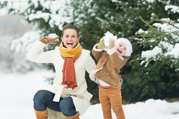 Feliz madre y bebé lanzando bolas de nieve en el parque de invierno — Foto de Stock