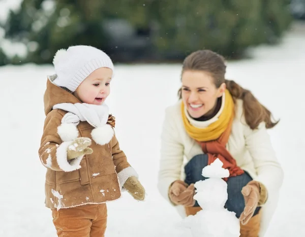 Feliz madre y bebé haciendo muñeco de nieve en el parque de invierno — Foto de Stock